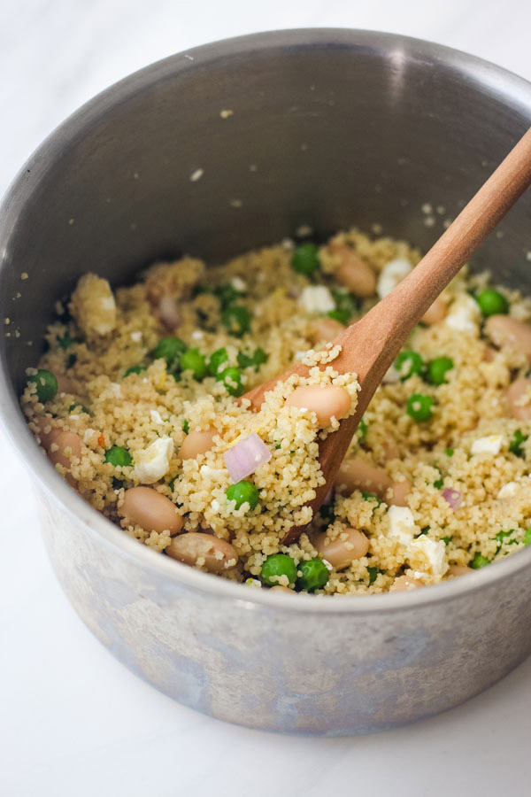 A metal pot with cooked couscous and a wooden spoon.