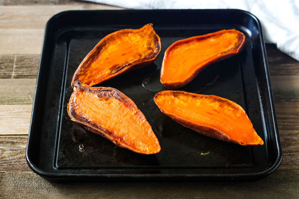 Baked sweet potato halves on a dark roasting pan.