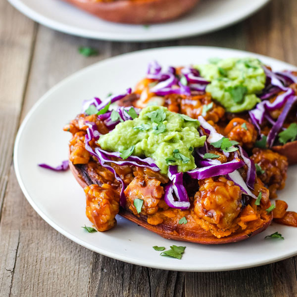 Tempeh stuffed sweet potatoes on white plates on a wood background.