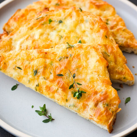 Triangles of cheesy toast on a blue plate with fresh thyme leaves sprinkled on top.