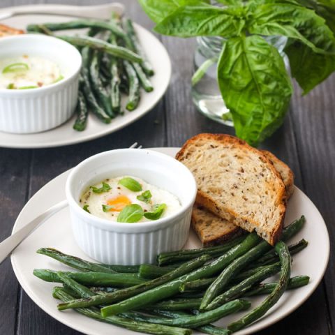 A white plate filled with green beans and a small ramekin with a baked egg.