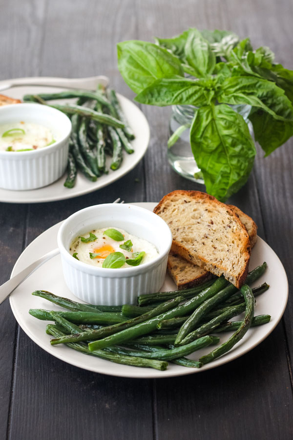 A white plate filled with green beans and a small ramekin with a baked egg.