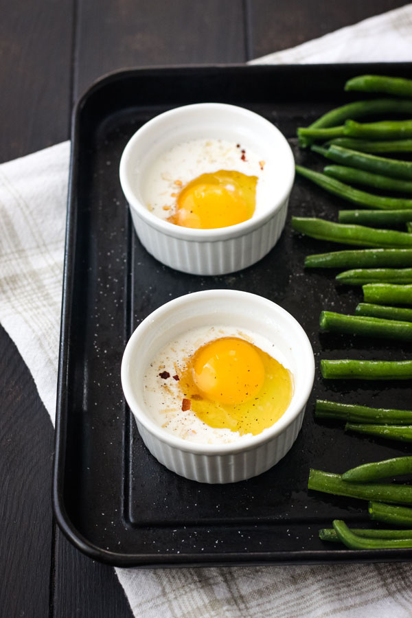 A toaster oven baking sheet with green beans and egg and cream-filled ramekins.