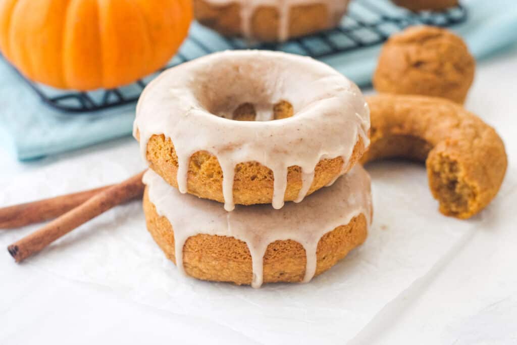 Glazed donuts stacked next to a mini pumpkin and cinnamon sticks.