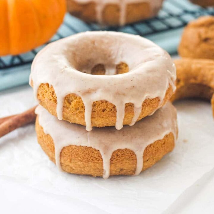 Glazed donuts stacked next to a mini pumpkin and cinnamon sticks.