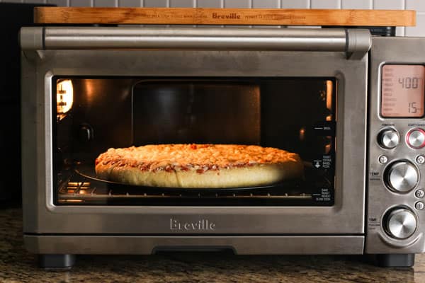 Pizza on pan cooking inside a toaster oven.