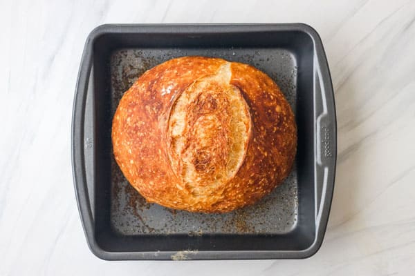 Round bread loaf inside a square metal pan.