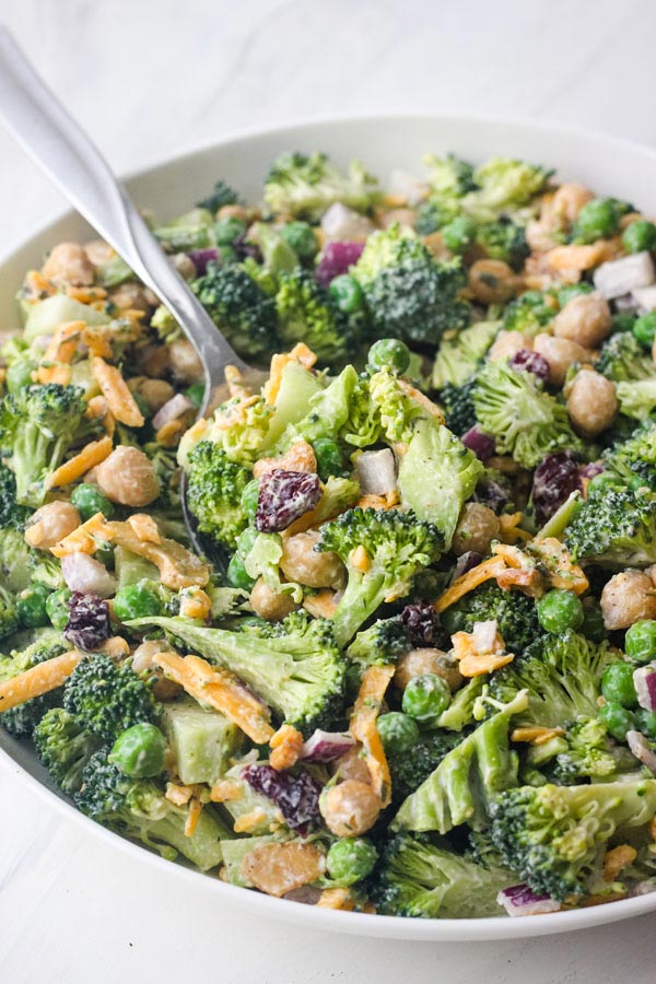 A white bowl with salad and a large metal serving spoon.