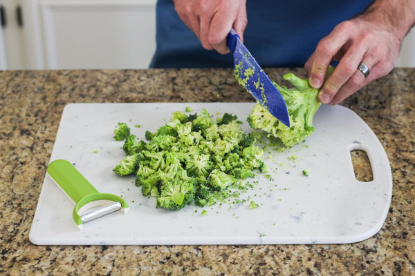 Person holding a broccoli stem and cutting florets onto a cutting board.