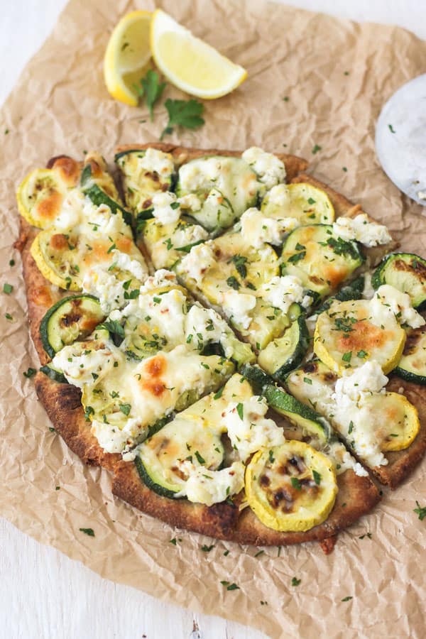 Broiled Zucchini and Lemon Ricotta Flatbread Sliced Into Pieces With Lemon Wedges