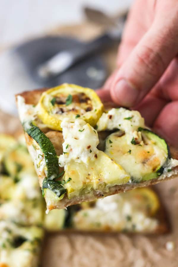 Hand holding slice of flatbread pizza.