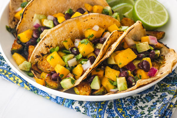 A white plate with tacos and lime wedges on a blue napkin.