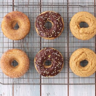 Plain, cinnamon sugar and chocolate topped donuts on a metal cooling rack.