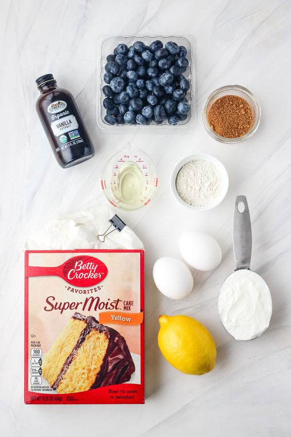 Boxed cake mix, fresh blueberries, eggs, yogurt and lemon on a table.