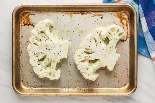 Seasoned cauliflower steaks on quarter sheet pan.