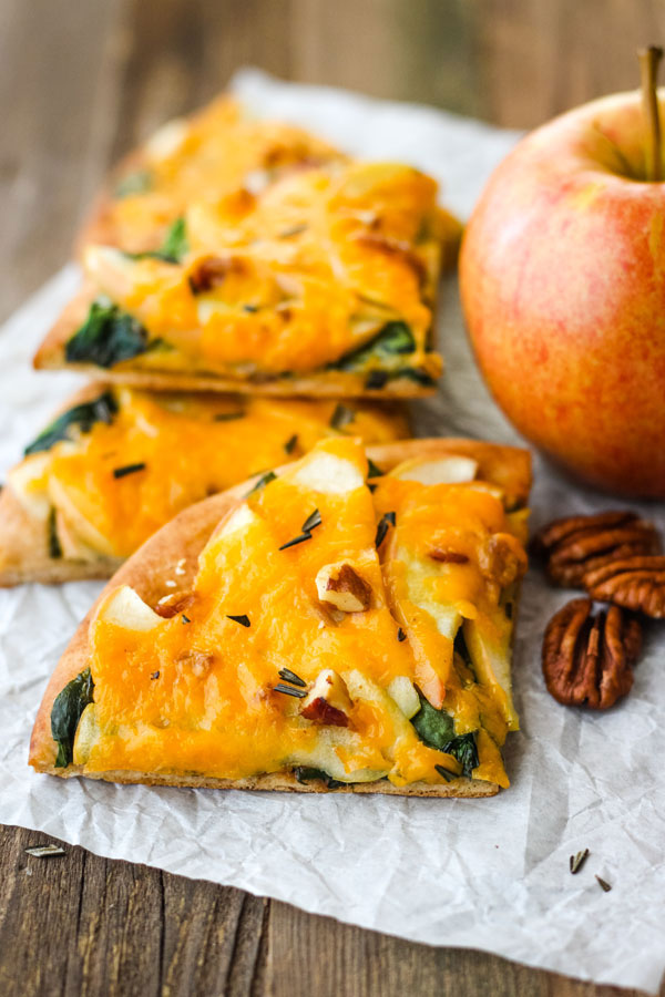 Pita pizza slices next to an apple and pecan pieces.