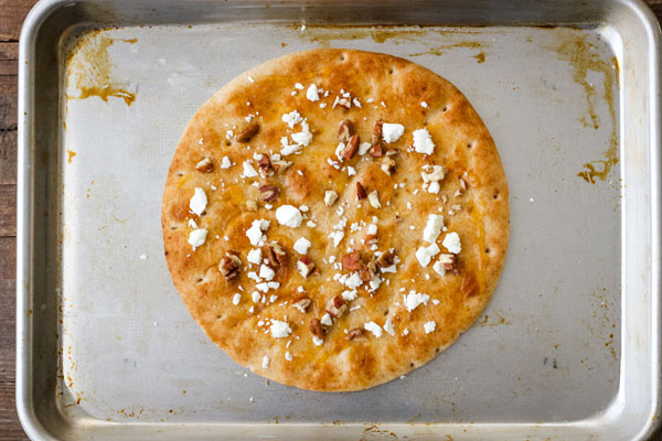 Pita bread on a baking sheet topped with preserves, nuts, and cheese.
