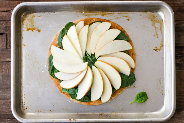 Pita on a baking sheet with apple slices fanned in a spiral shape.