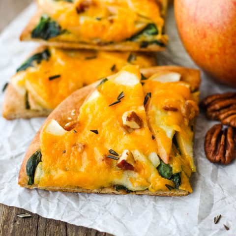 Pieces of Cheddar Apple Pita Pizza with an apple and pecans.