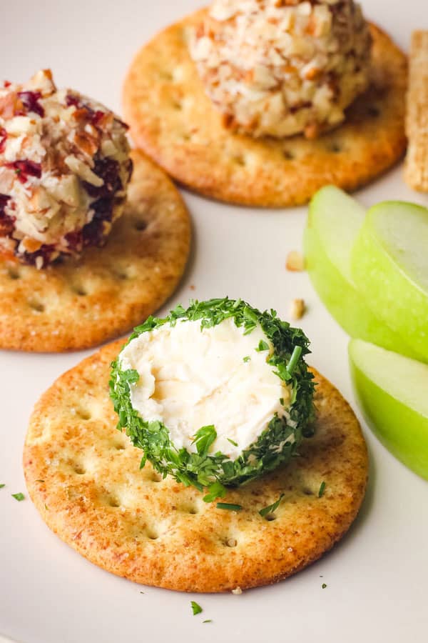 Closeup of creamy cheese in an herb-coated ball on a cracker.