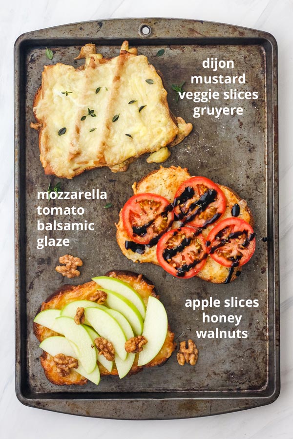 Three toasts on a sheet pan with toppings including apple slices, tomato, and vegetarian sandwich slices. 