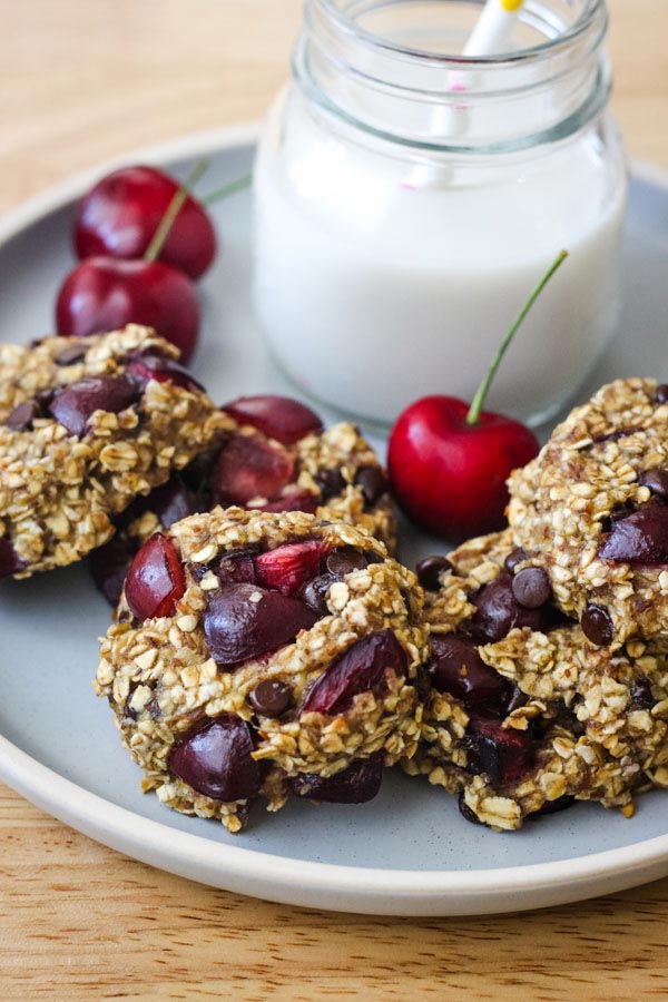 A blue plate with oat cookies, fresh cherries, and a glass of milk.