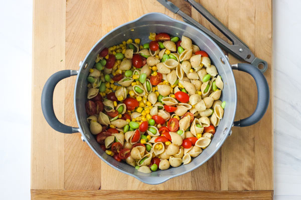 Chickpea pasta, tomatoes, and edamame in a pot on a cutting board.