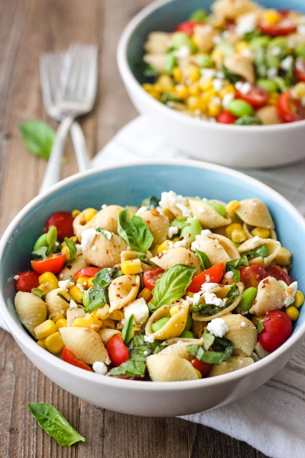 Closeup of pasta salad in two blue bowls on a wood table with two forks.