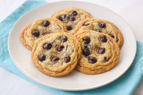 Five chocolate chip cookies on a white plate with a blue napkin.