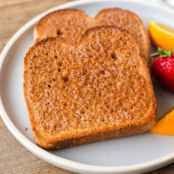 Two slices of cinnamon toast on a blue plate with fruit.