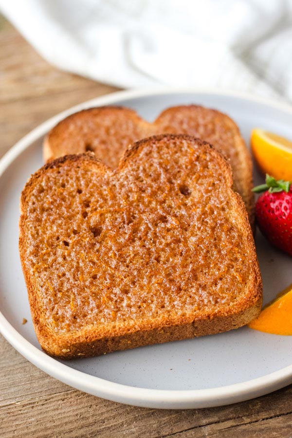 Slices of cinnamon toast on a blue plate with strawberries and orange slices.