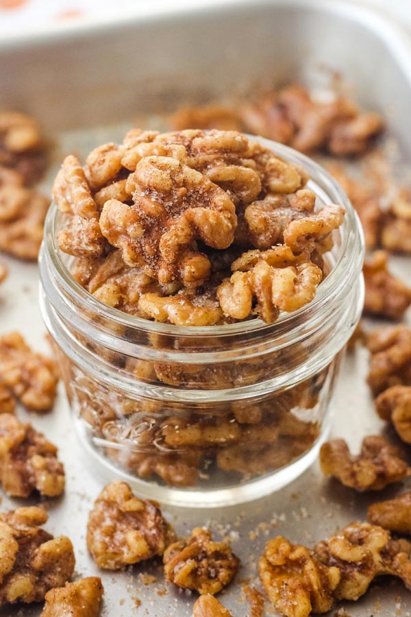 A small mason jar of cinnamon walnuts overflowing onto a sheet pan.