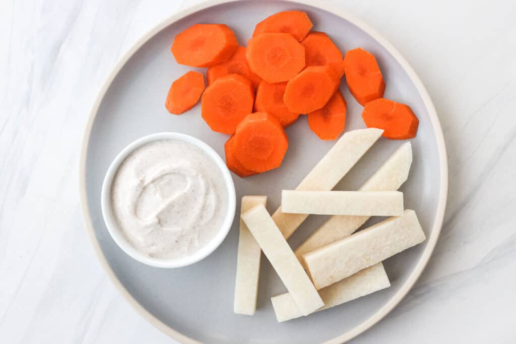 Ramekin with dip on plate with carrot slices and jicama sticks.
