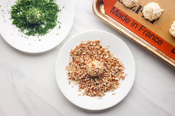 Cheese ball rolled in chopped nuts on plate.