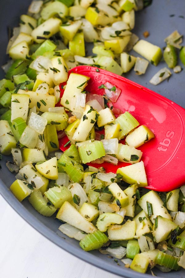 Diced apple, onion, and celery cooked in a skillet with a red spatula.