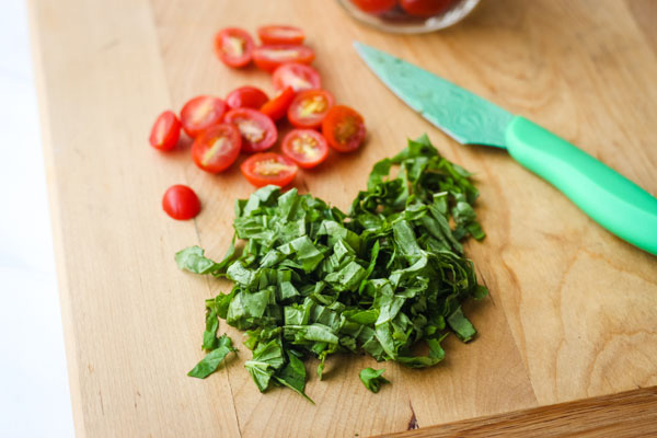 Sliced tomatoes and basil on a cutting board.