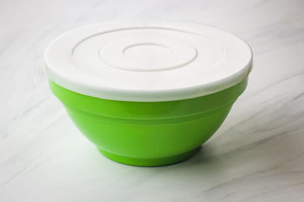 Green mixing bowl covered with a plastic lid.