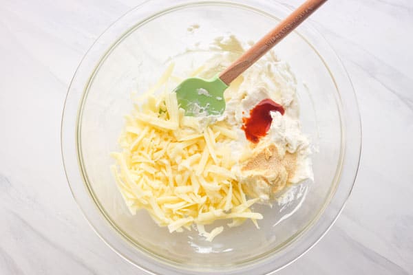 Glass bowl with cream cheese, shredded cheese, and seasonings.