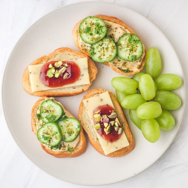 Overhead view of plate with topped toasts and green grapes.