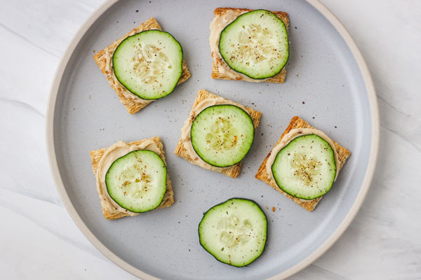 Cucumber and hummus topped crackers on a blue plate.