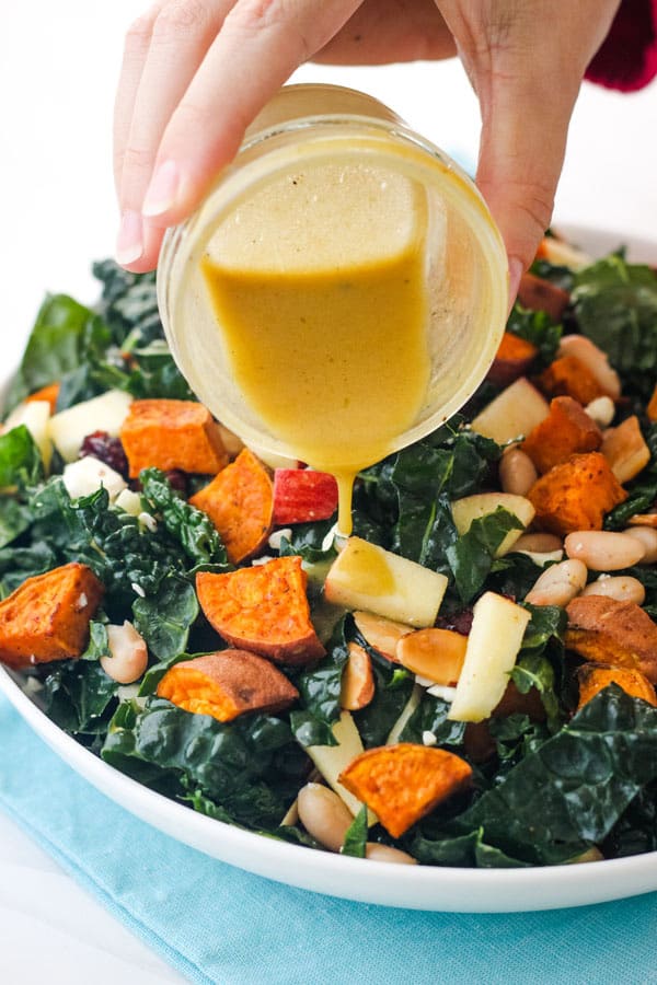 Hand pouring vinaigrette onto a kale salad.