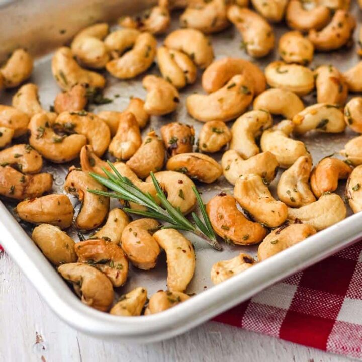 Closeup of small pan with roasted nuts and sprig of fresh rosemary.