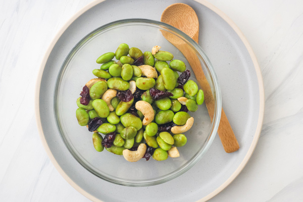 Edamame salad in a glass bowl with a wooden spoon.