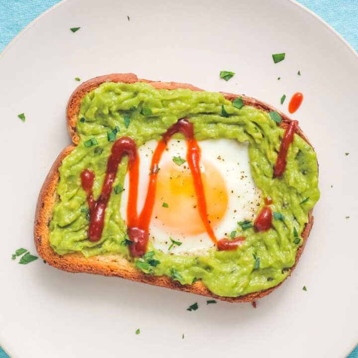 Overhead view of an egg cooked on a piece of toasted bread topped with avocado and hot sauce.