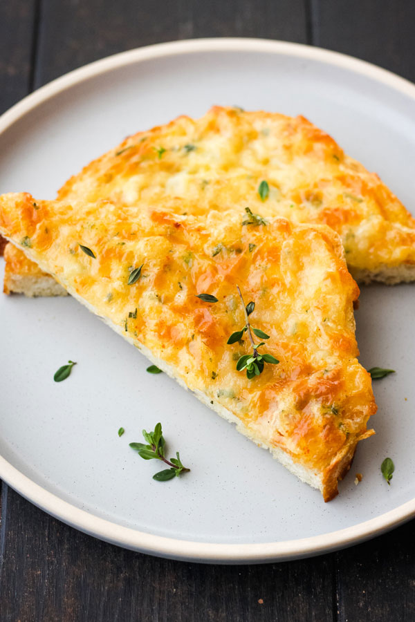 Cheese toast triangles on a blue plate sprinkled with fresh thyme.