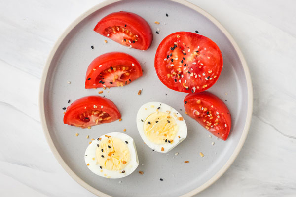 Hard boiled egg and tomato slices on a blue plate.