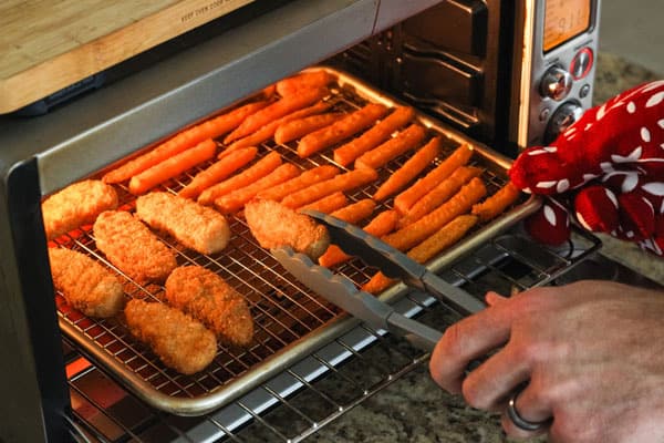 Man using tongs to flip meatless nuggets on a rack.