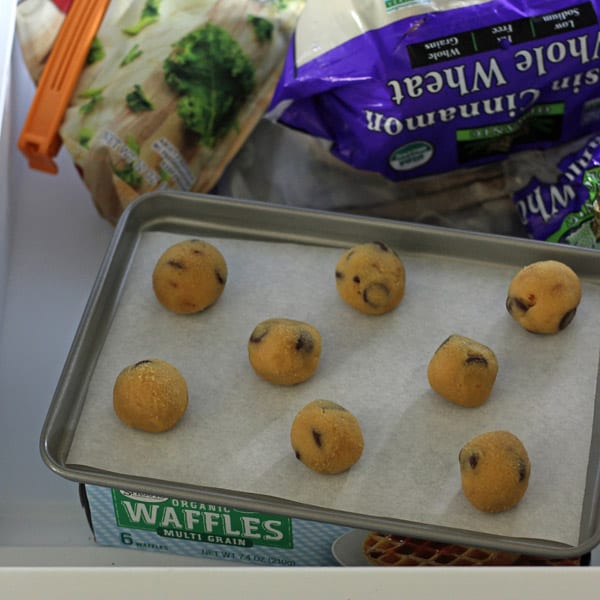 Lined sheet pan of cookie dough balls inside a freezer.