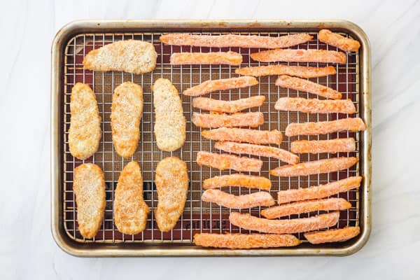 Frozen vegan chicken strips and sweet potato fries on a rack.