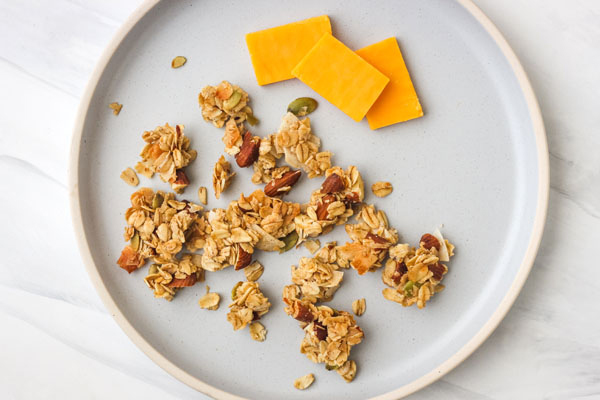 Chunky granola and cheddar cheese slices on a blue plate.